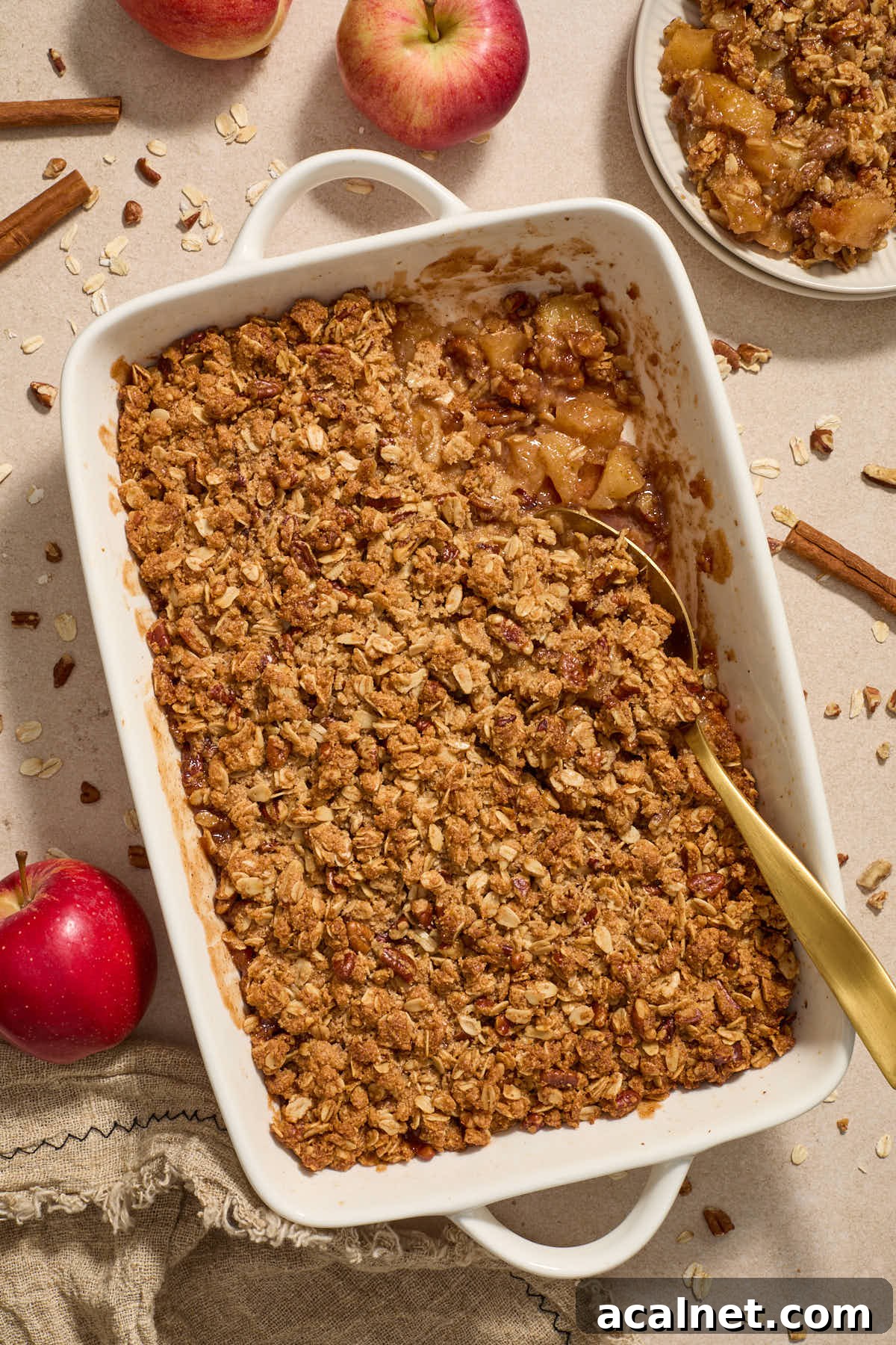 Apple crisp in baking dish with serving spoon and some scooped out on a plate to the side.
