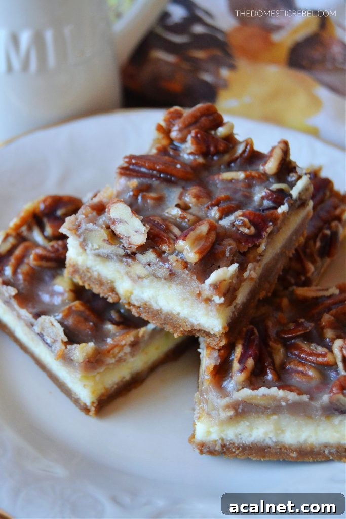 Pecan Pie Cheesecake Bars Recipe 3 pecan pie cheesecake bars stacked and arranged on a gold-rimmed plate. they're sitting on a floral fall-themed dish towel with a milk jug in the background.