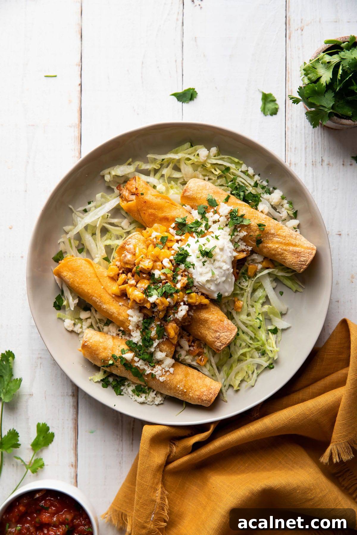 plate of taquitos filled with chicken and mexican corn served with lettuce and sour cream on top