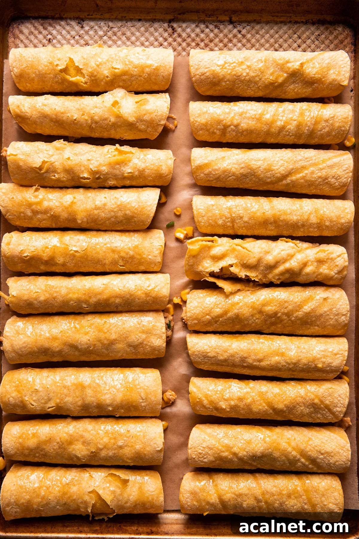 two rows of taquitos on a baking sheet before being baked