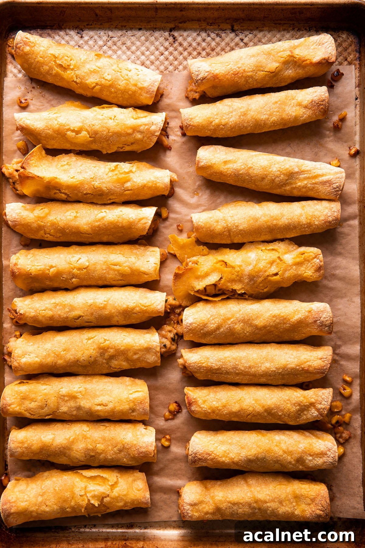 two rows of taquitos on a baking sheet after being baked