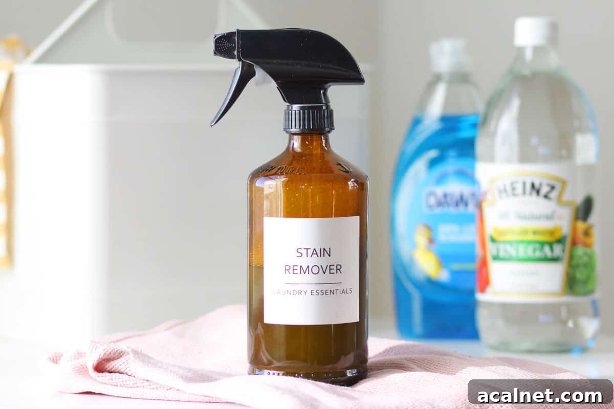 Homemade Laundry Stain Remover Spray Recipe 3 a glass amber spray bottle with a label that says 'stain remover laundry essentials' and a bottle of dawn dish soap and a bottle of distilled vinegar behind it