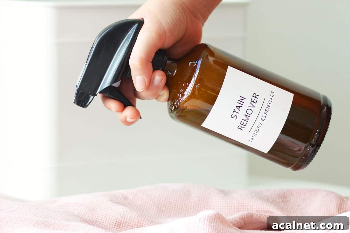 Homemade Laundry Stain Remover Spray Recipe 4 a glass amber spray bottle with a label that says 'stain remover laundry essentials' on it being sprayed at a stained baby outfit