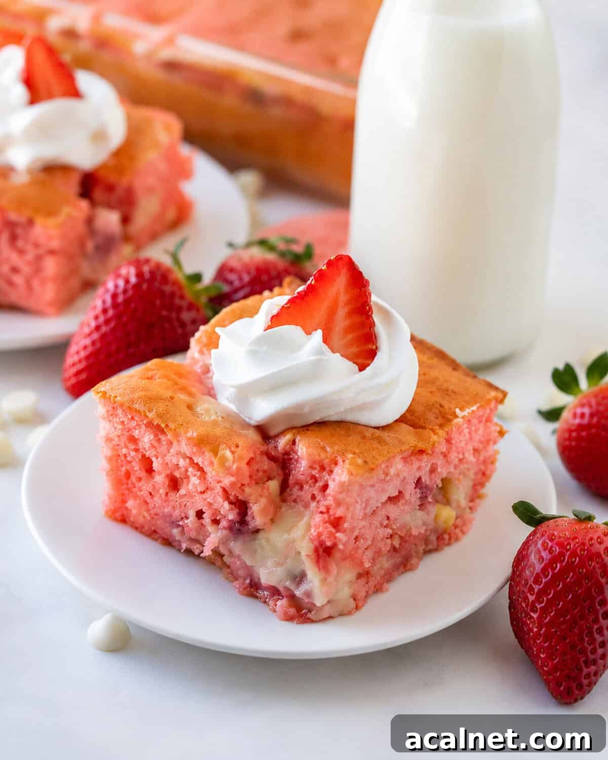 A slice of strawberry earthquake cake topped with whipped cream and a fresh strawberry on a plate.