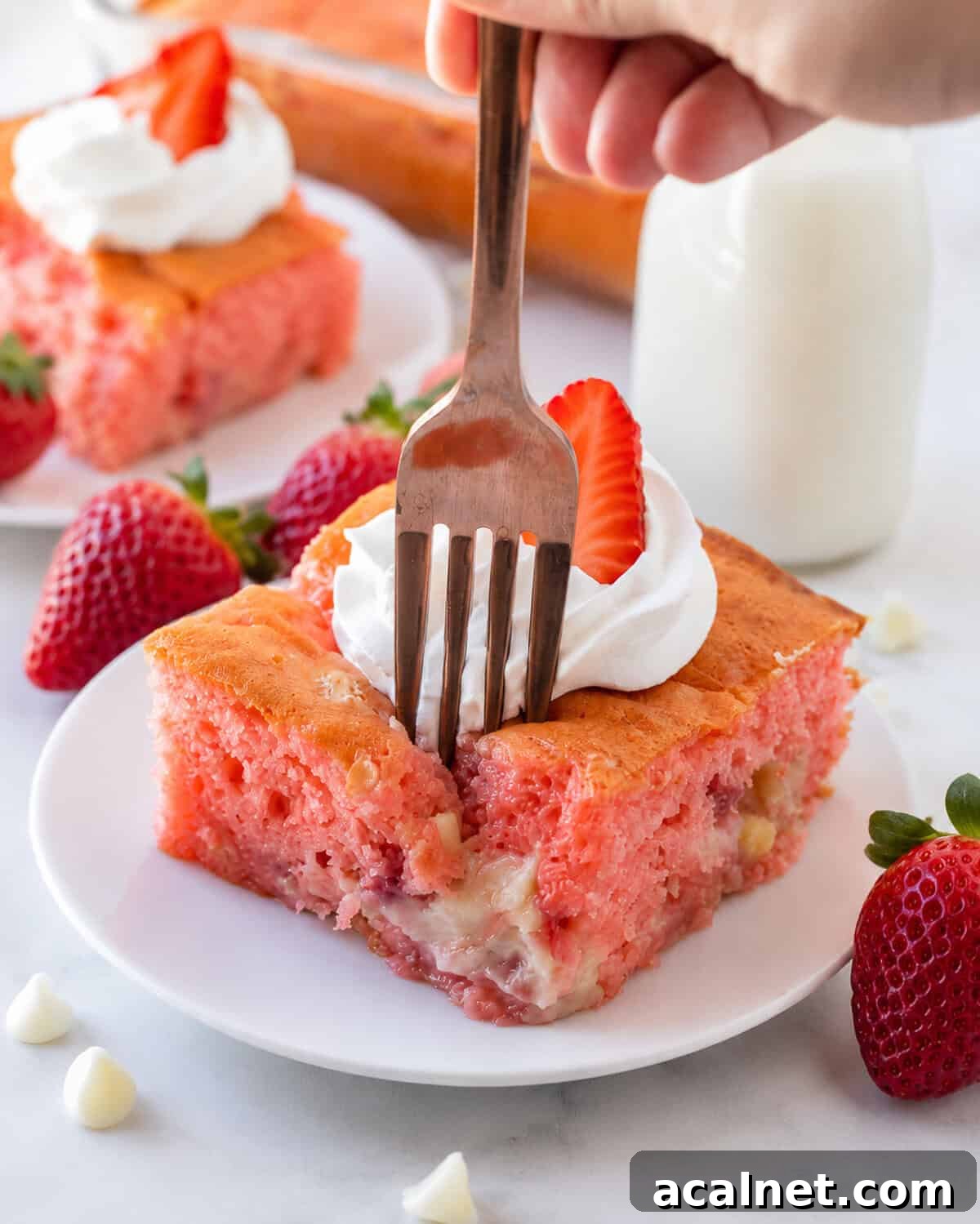 A fork taking a bite of a slice of strawberry earthquake cake.