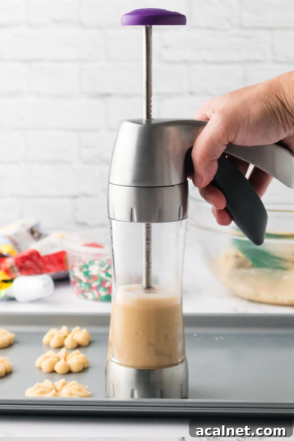 Classic Christmas Spritz Cookie Recipe 10 holding cookie press above cookie sheet