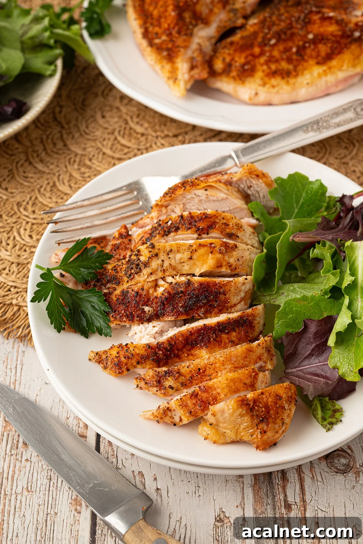 Sliced oven-roasted split chicken breast showing juicy meat and crispy Texas dry rub skin, garnished with fresh chopped parsley on a white plate.