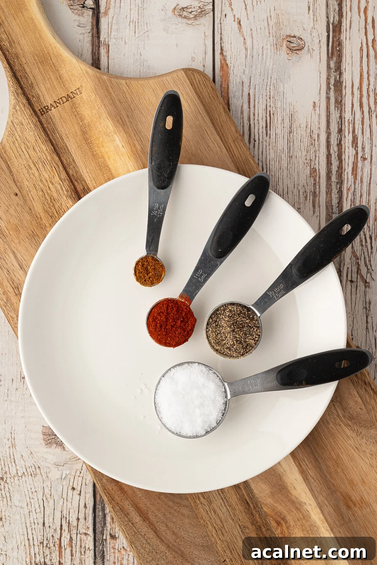 Individual spoons of spices including paprika, garlic powder, salt, and black pepper laid out to make a savory Texas dry rub for chicken.