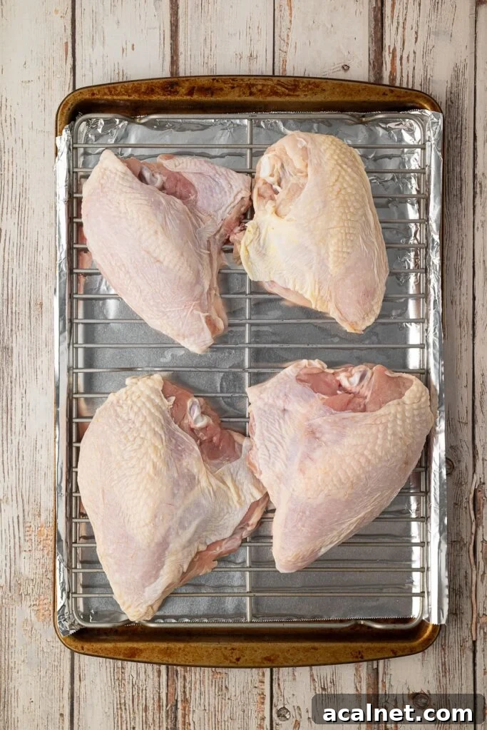 An overhead shot showing how to place the split chicken breasts on a rack fit over a foil lined baking sheet.