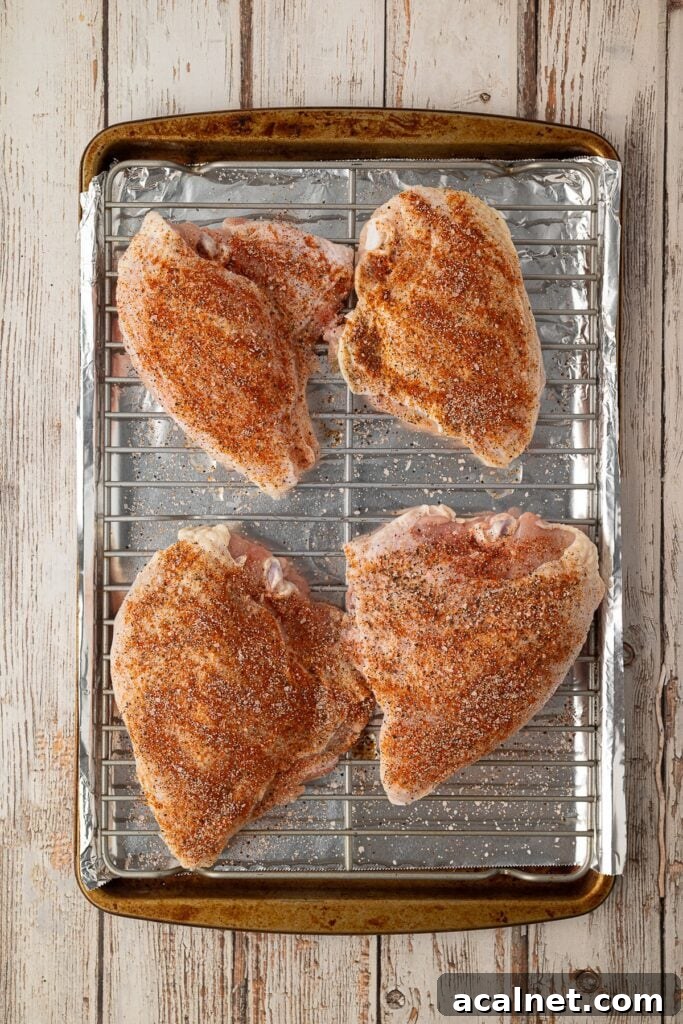 Seasoned bone-in chicken breasts arranged evenly on a lined baking sheet ready to be roasted.