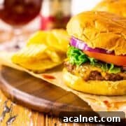 Juicy venison burger on a wood platter with potato chips.