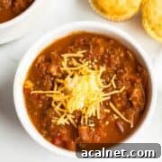 A bowl of chili with shredded cheese one top.