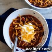 Spicy venison chili in a white bowl, topped with sour cream and shredded cheese.