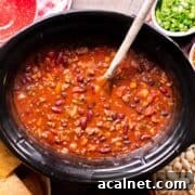 A black slow cooker filled with venison chili.