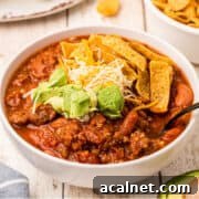 A white bowl filled with venison chili, topped with tortilla strips, shredded cheese, and avocado slices.