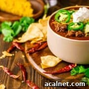A bowl of venison chili topped with sliced jalapeno, sour cream, and shredded cheese.