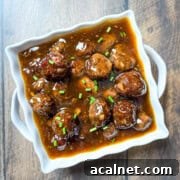 Sweet and Sour Venison Meatballs simmering in white baking dish, showing glossy sauce coating each meatball.