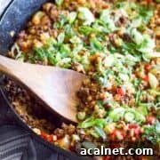 A skillet of keto cauliflower rice being mixed with a wooden spoon