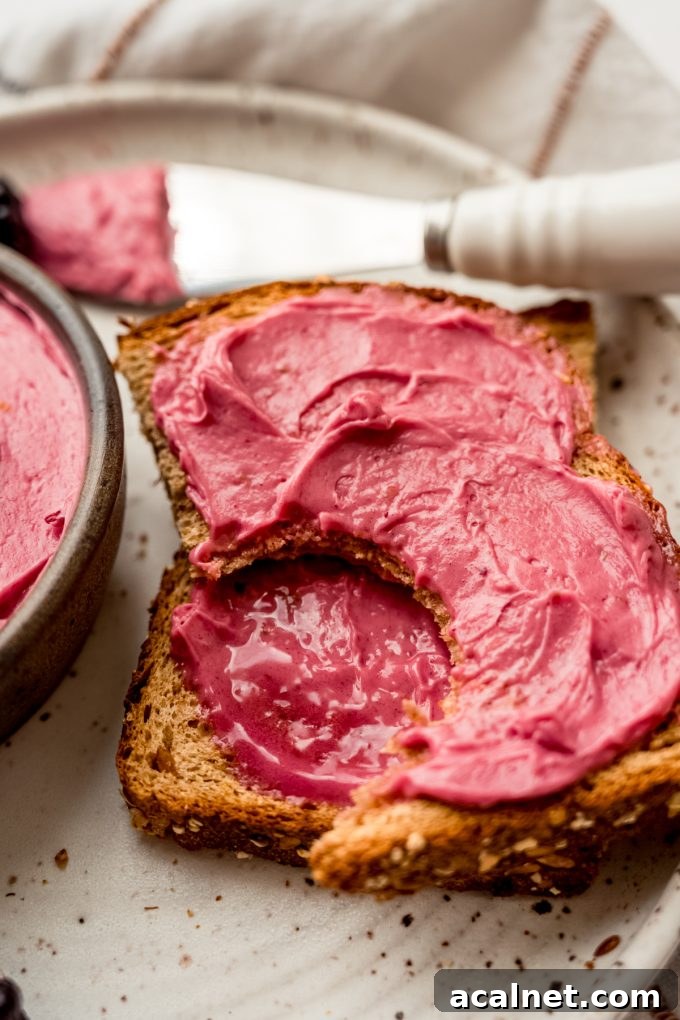 A slice of toast spread with blackberry butter and a bite has been taken out of one of the pieces of the toast.