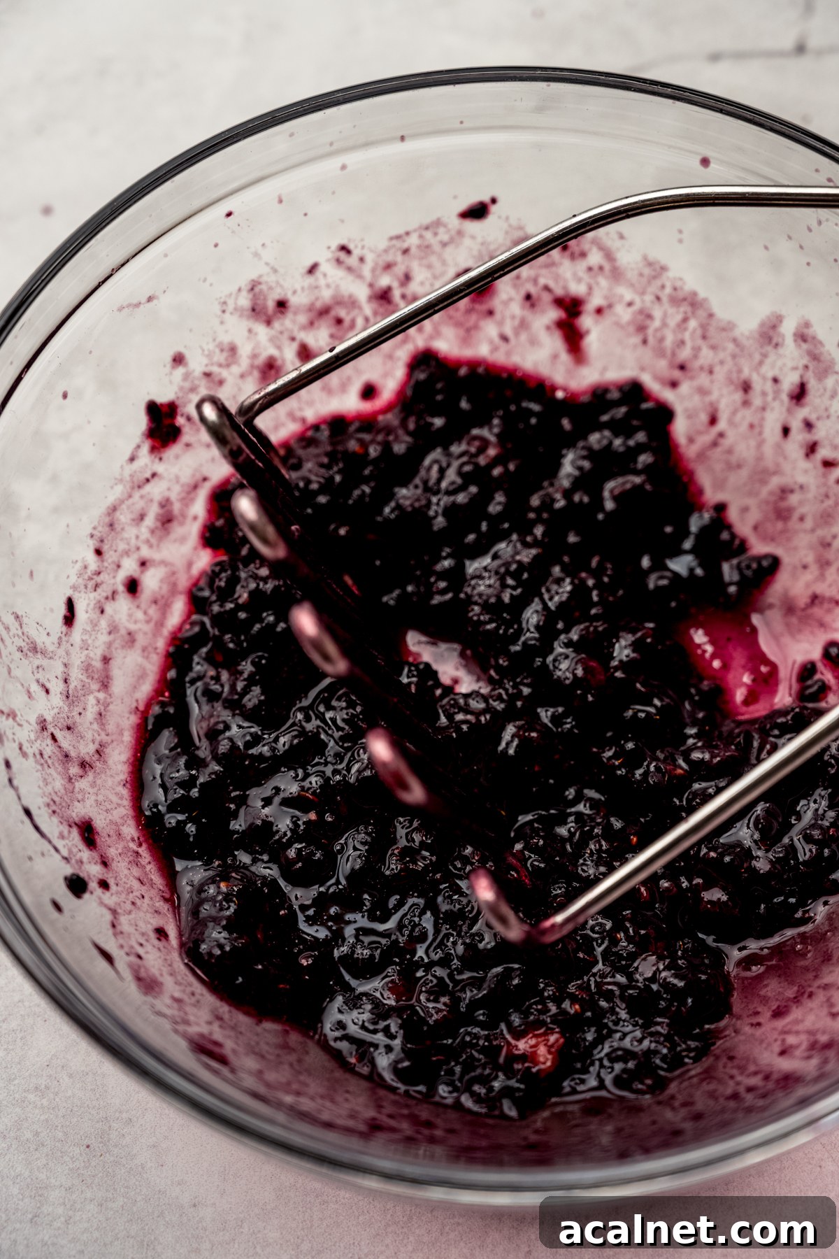 Blackberries in a bowl being macerated with a potato masher.