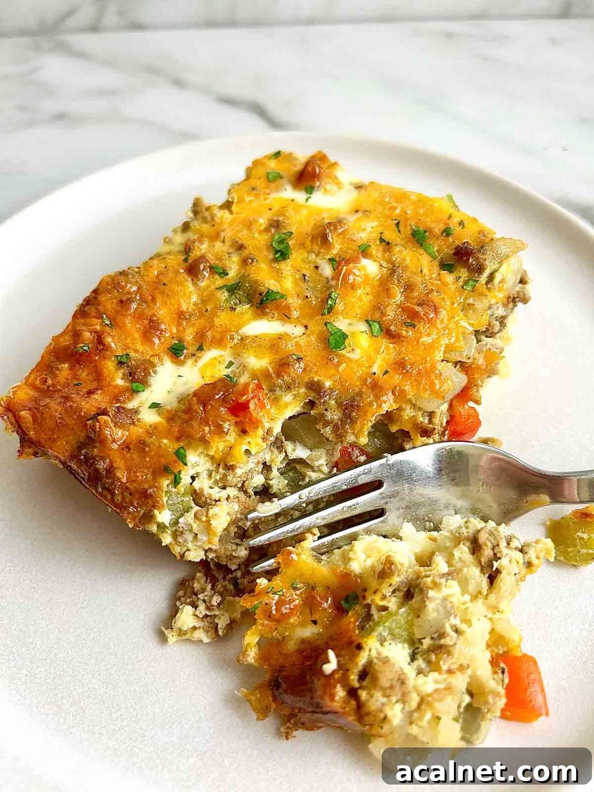 Hearty Breakfast Casserole with Sausage and Cheese 2 fork cutting off chunk of breakfast casserole on plate.