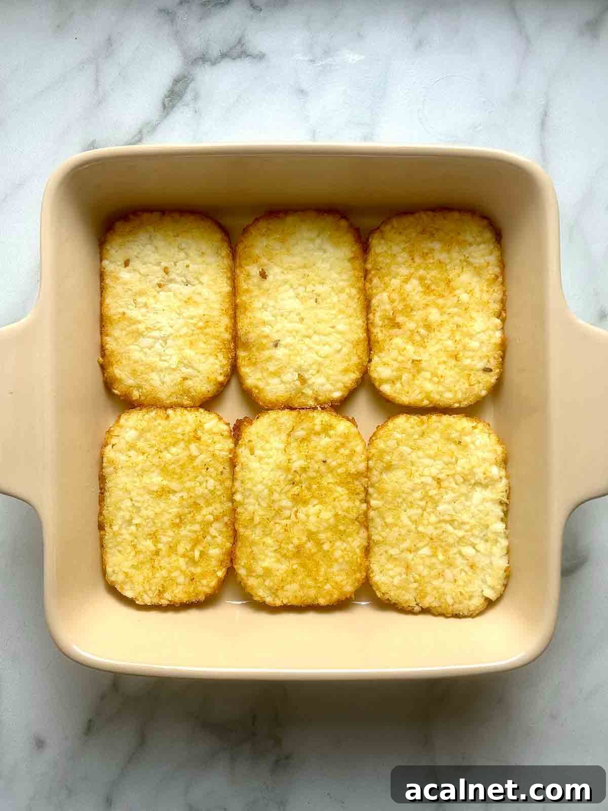 Hearty Breakfast Casserole with Sausage and Cheese 4 hashbrown patties arranged on bottom of baking dish.