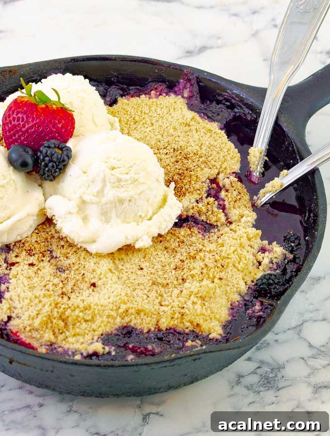 Grilled Triple Berry Crisp in a Cast Iron Skillet with three scoops of ice cream and berries