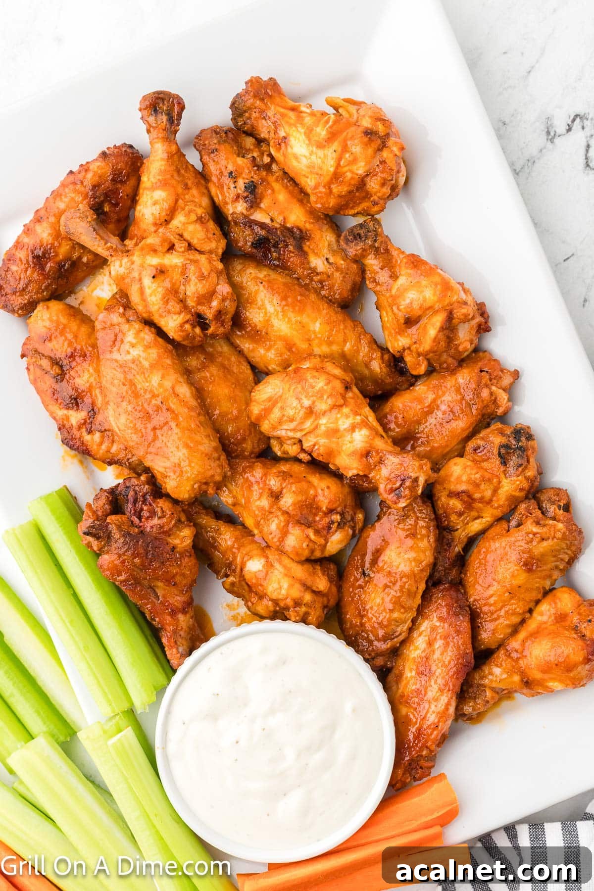 Smoked Chicken Wings stacked on a white platter with a side of celery sticks and carrots and a bowl of ranch dressing