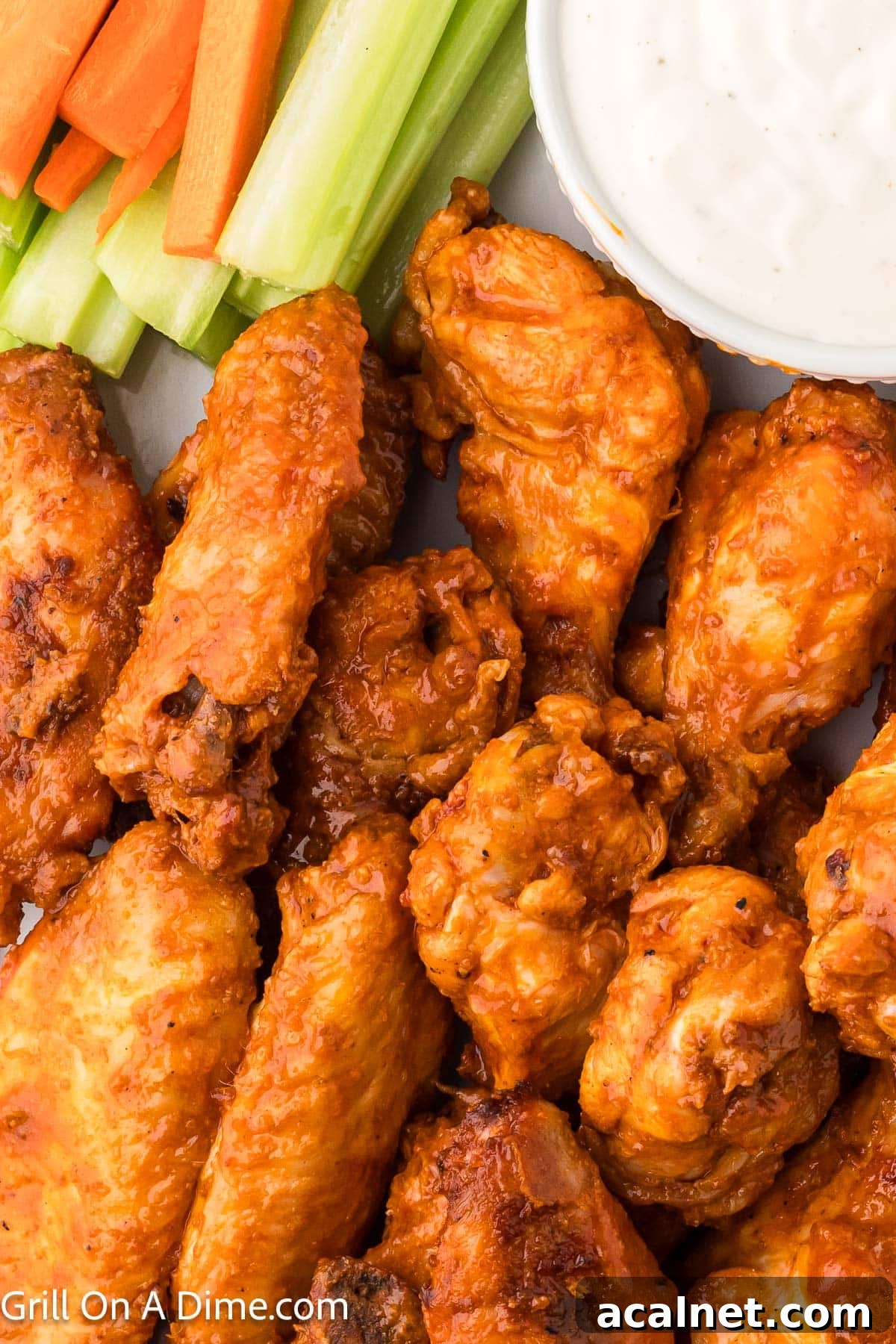 Buffalo Chicken Wings stacked on a white platter with a side of celery and carrots and a bowl of ranch dipping sauce