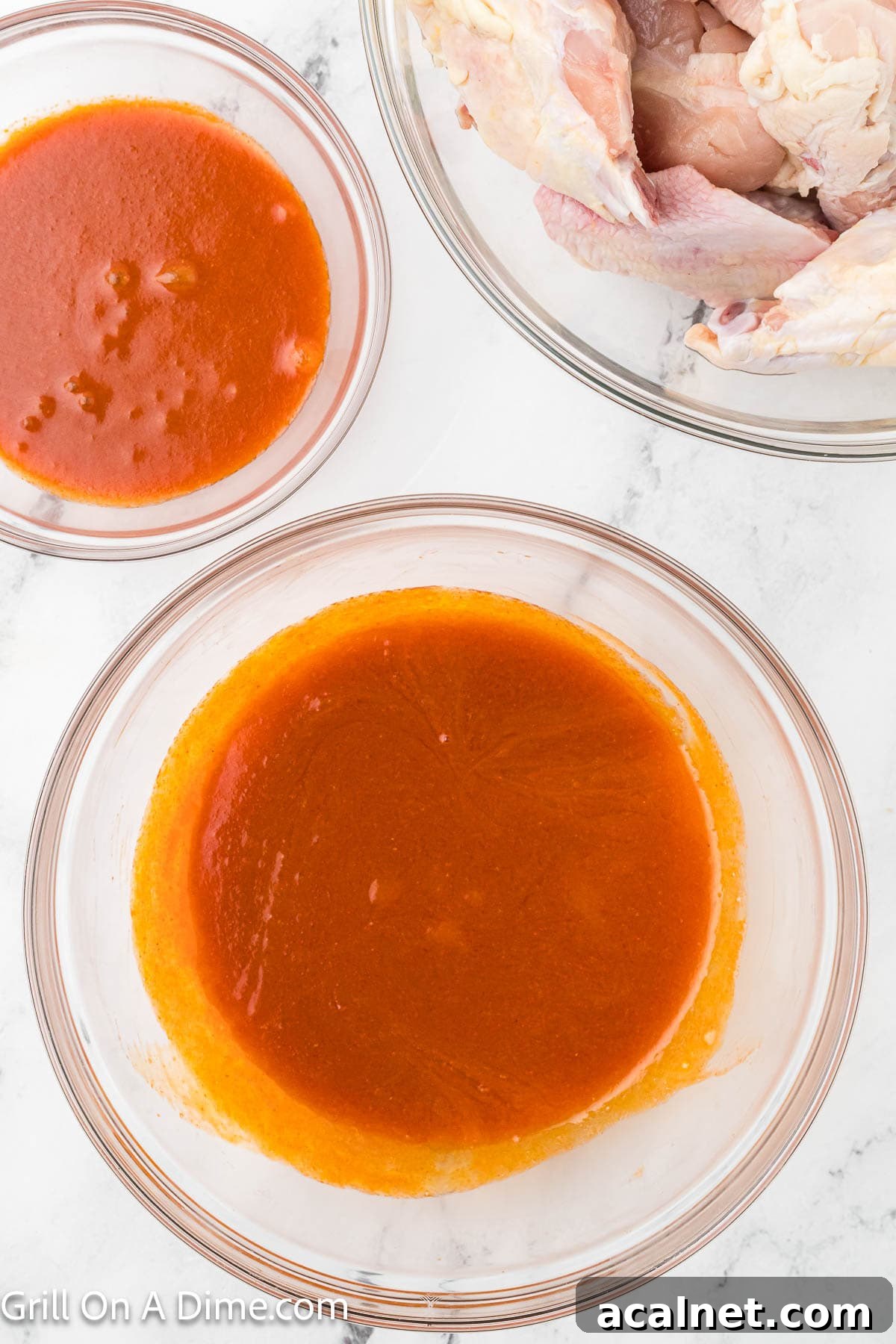 Buffalo Sauce mixture in a large bowl and some in a smaller bowl with a bowl of uncooked chicken wings on the side