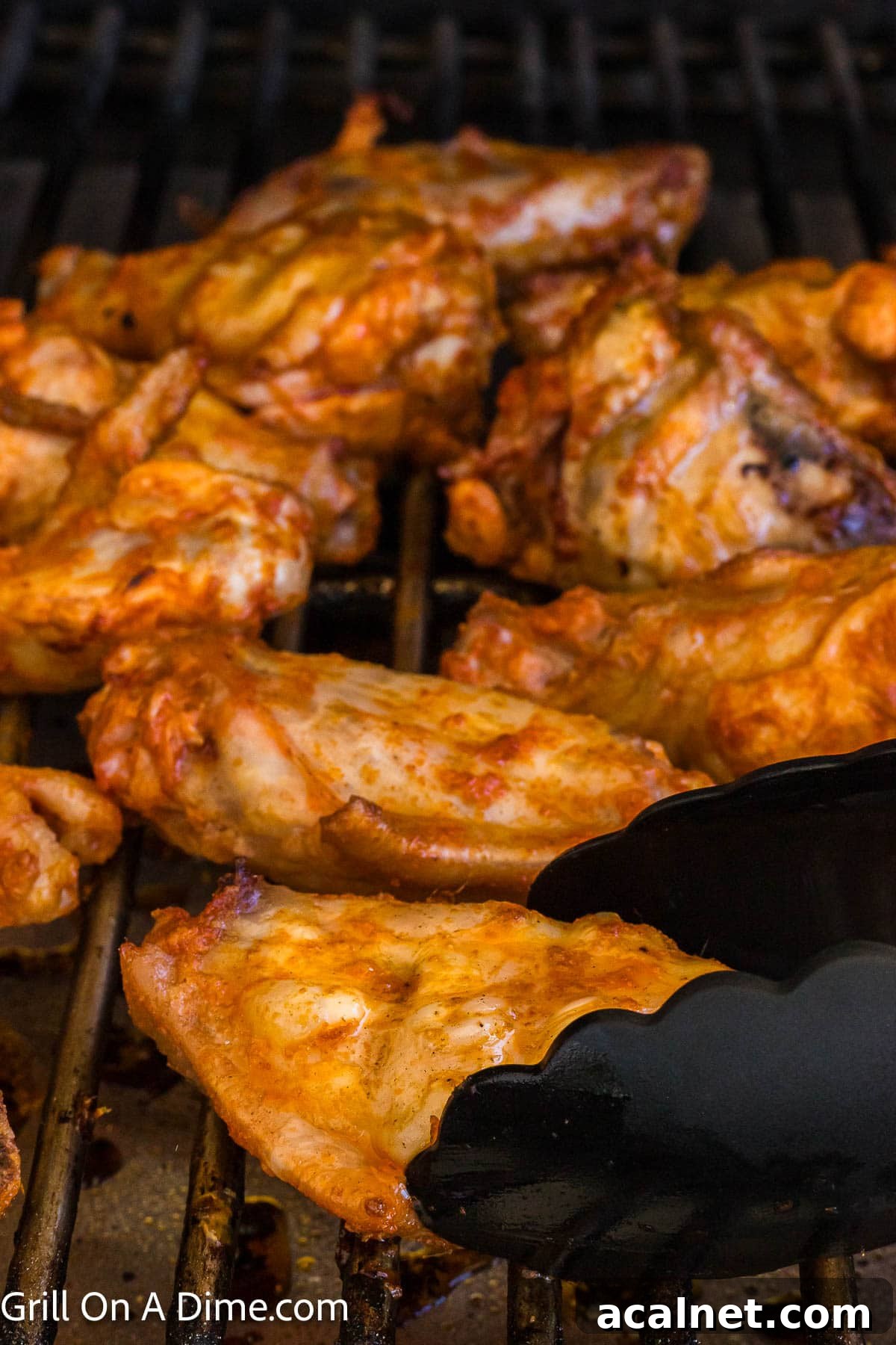 Cooked chicken wings on the grill grates with one being held with tongs